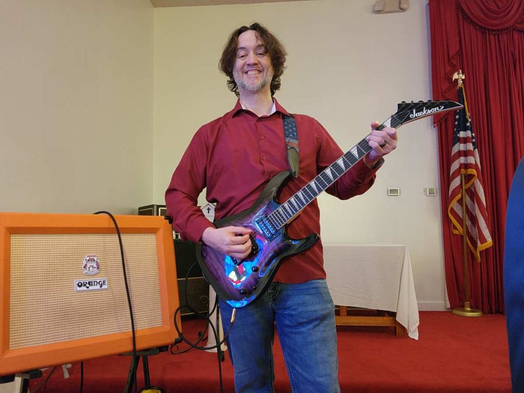 Eric Hepperle playing purple starburst Jackson electric guitar through Orange Crush 60W amp on stage at St. Elizabeth church.